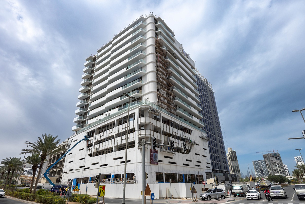 Pearl House By Imtiaz A multi-story building under construction with scaffolding, surrounded by palm trees and vehicles on the road.